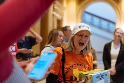 A woman in an orange shirt chants inside the Capitol.