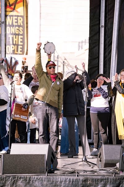 A large group of musicians perform on an outdoor stage at a huge rally