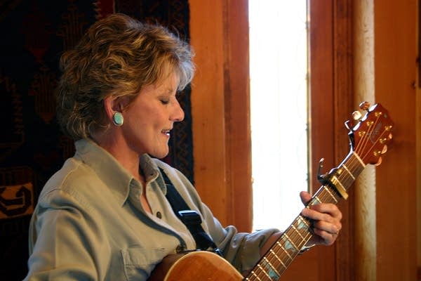 A woman smiles and strums a B-flat chord on a guitar