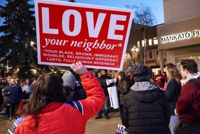 A demonstrator holds a large red sign reading, "LOVE your neighbor."