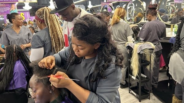 A busy hair salon, where the braiders all wear matching gray shirts.