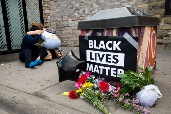 Three people hug near a memorial.