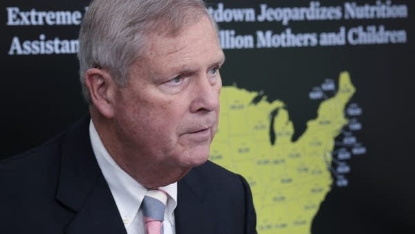 Secretary of Agriculture Tom Vilsack stands in front of a presentation at a press briefing
