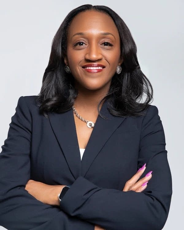 A woman in a suit poses for a photo in front of a gray background.