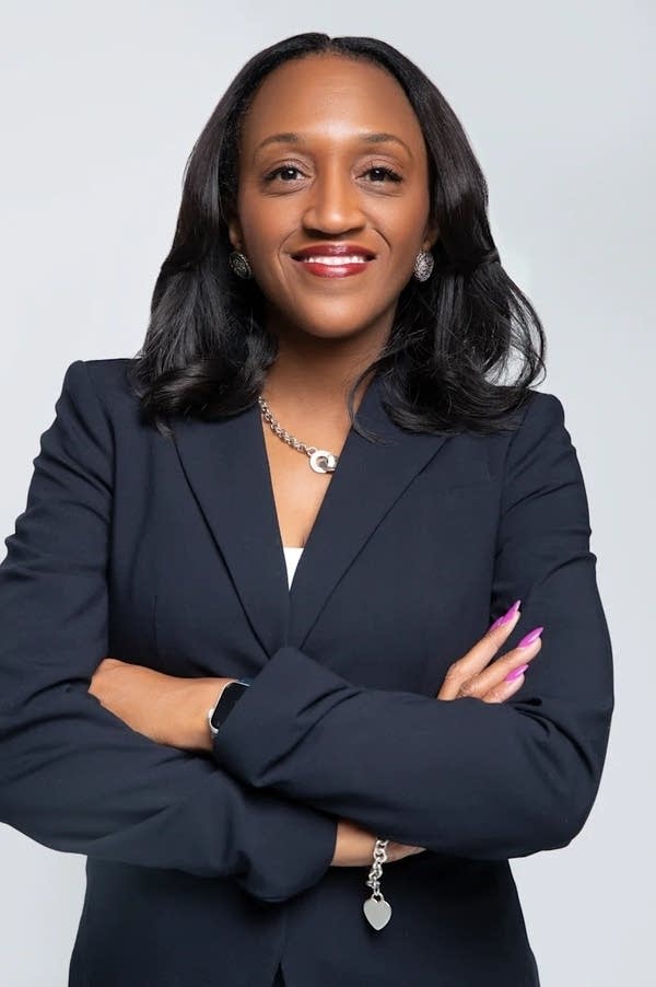 A woman in a suit poses for a photo in front of a gray background.
