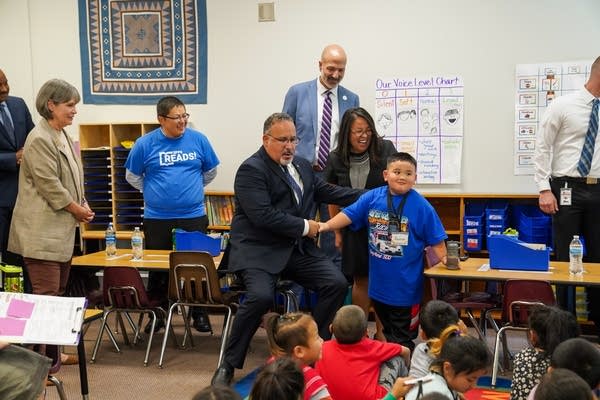 A man in a suit shakes a student's hand.