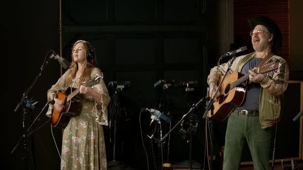 Two musicians sing and play guitars in a recording studio
