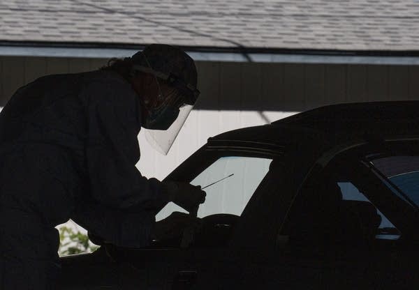 A person wearing PPE and holding a nasal swab in silhouette.