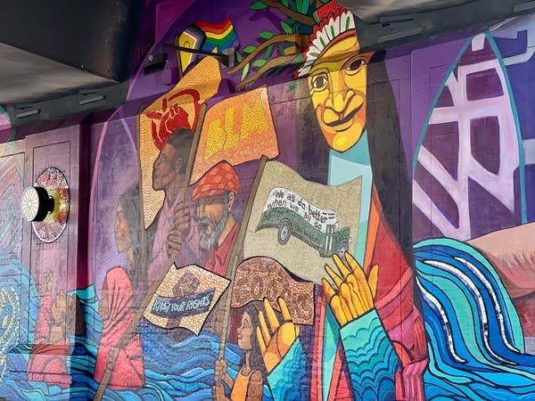 A mural on the wall with rich colors shows protestors of many different backgrounds.