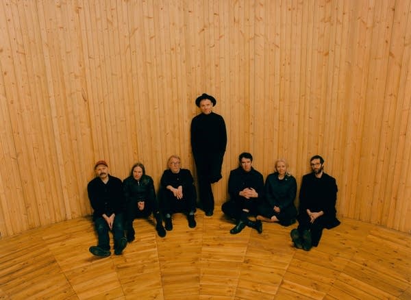 Seven people sitting in a circular room paneled and floored in hardwood