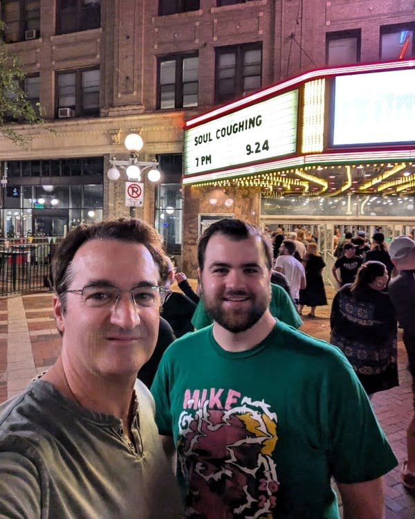 Two men stand in front of a theater marquee.