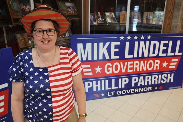 A woman in an American flag outfit stands next to a "Mike Lindell for Governor" sign.