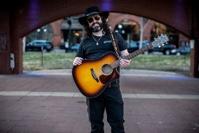 A man with a guitar stands on the outdoor stage at Mears Park
