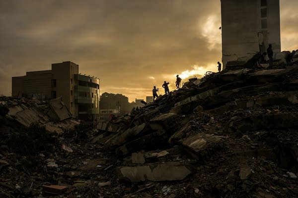 Silhouettes of three people are seen atop a mound of rubble at sunset.