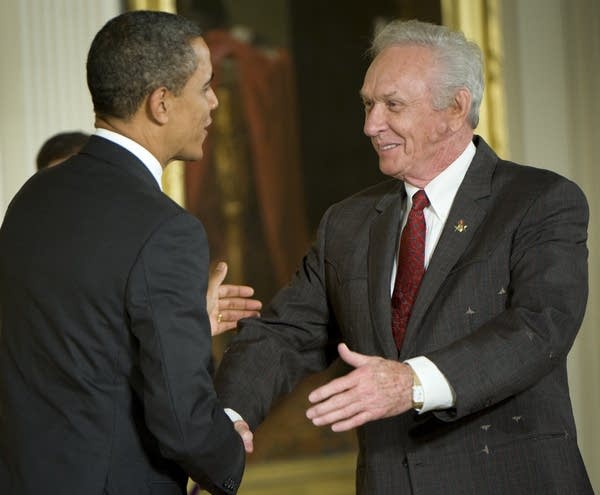 Two men smile and shake hands at an awards presentation ceremony