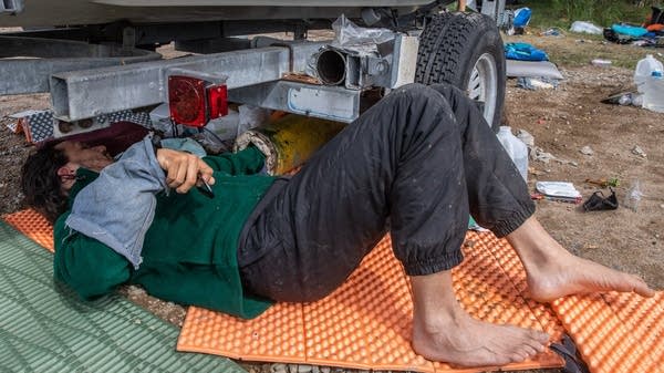 An activist lays on the ground under a boat trailer.