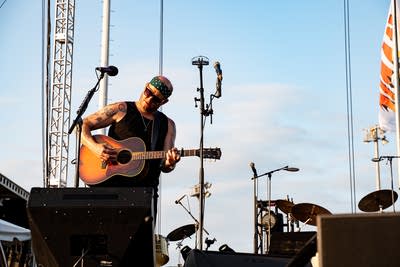 A musician sings and plays guitar on an outdoor stage