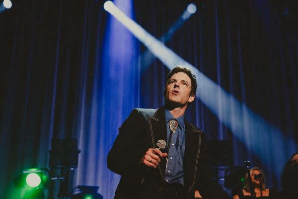 A musician sings onstage in a large music venue