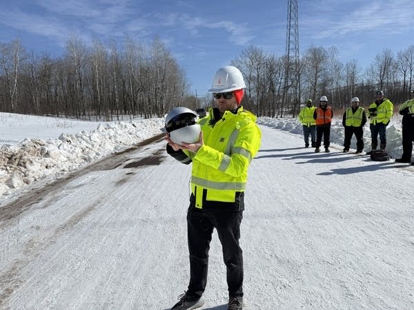 A utilities worker holds a large sized metal ball.