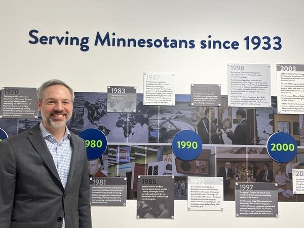 A man poses in front of a timeline display titled "Serving Minnesotans since 1933.