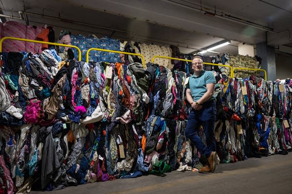 A man stands next to piles of used clothes in a warehouse