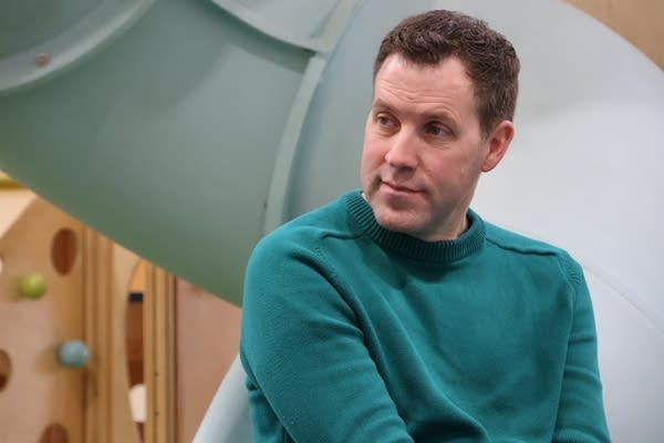 A man in a green shirt sits next to a children's playground.