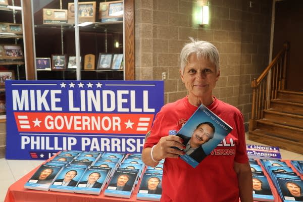 A woman poses next to a display of Mike Lindell books while holding one.