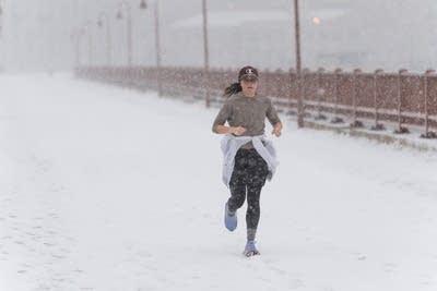 A woman jogs across a bridge during a snowstorm.