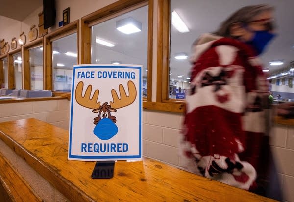 A woman walks past a sign saying face masks required. 