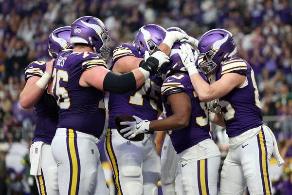 A group of Vikings football players celebrate in a huddle.