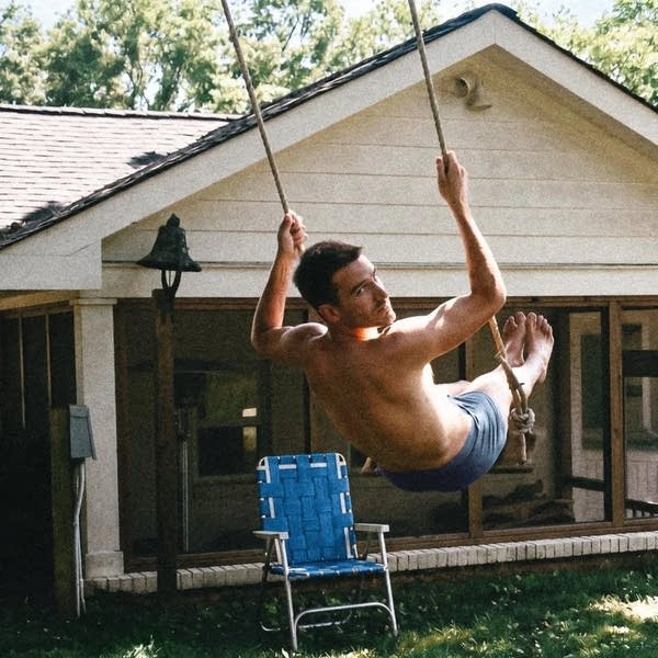 A man glides on a swing in front of a house in summer