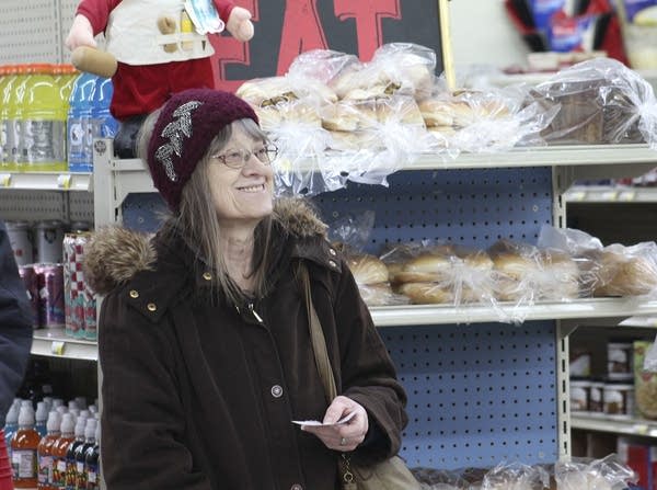 A person smiles as they stand beside a shelf of food.