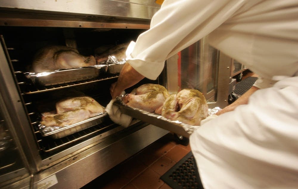 A chef places fresh turkeys in the oven