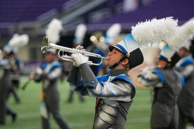 A marching band performs on the field of a football stadium.