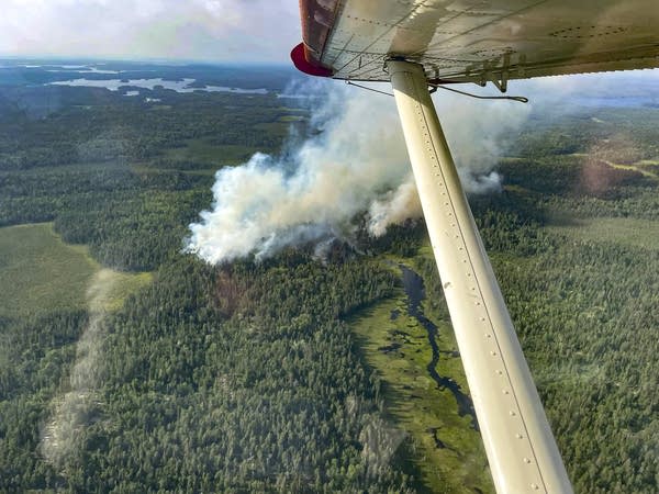 a forest fire is seen from an airplane with part of the plane wing visible in the photo