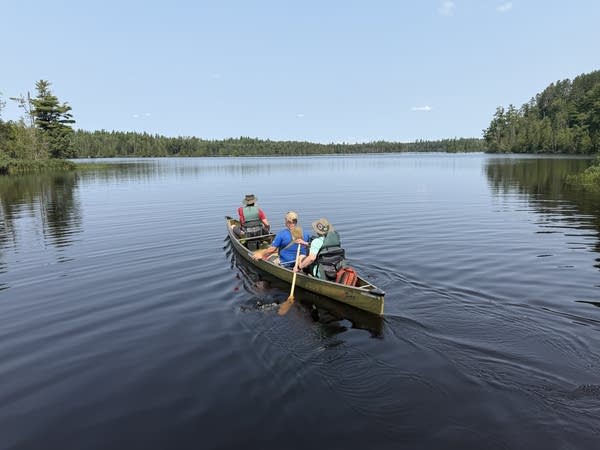 Three people in a canoe paddle out into a lake.