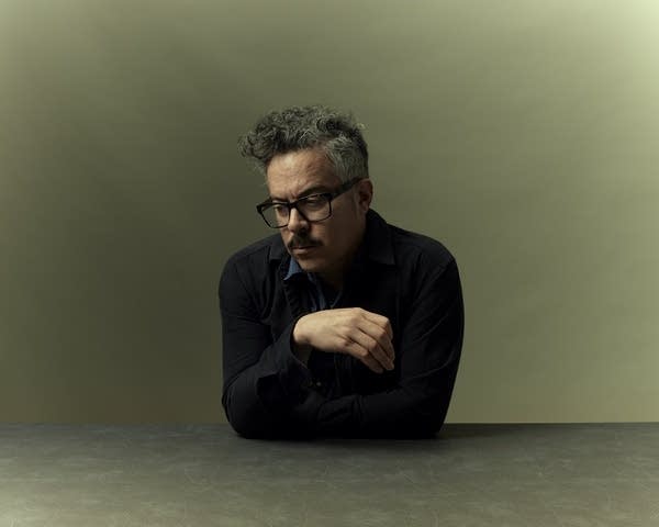 A man in a sweater and glasses poses thoughtfully for a portrait