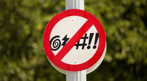 No Cursing Street Sign in front of a green bush