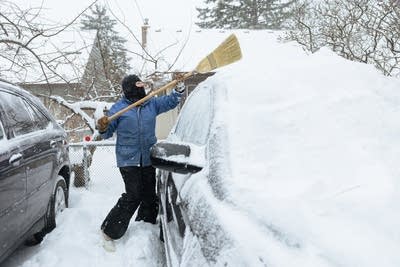 A woman uses a broom to clear snow off her car.