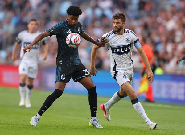 A soccer player traps the ball with his chest while pushing away another player.