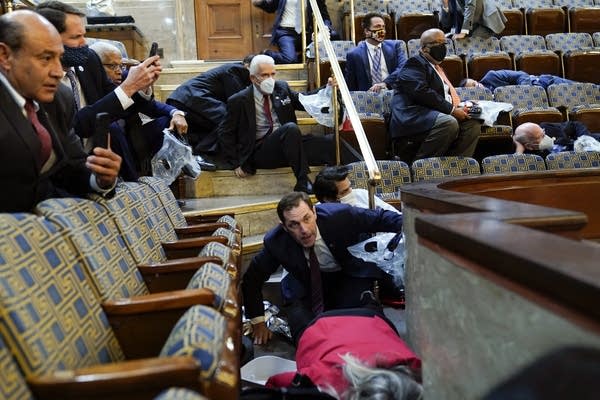 People shelter under furniture within the House Chamber.