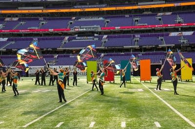 A marching band performs on the field of a football stadium.