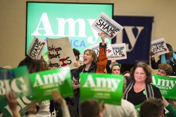 Protestors stand on a stage as others hold campaign signs in front of them