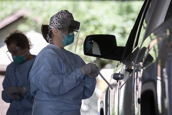 A person wearing PPE holds a swab while standing beside a truck. 