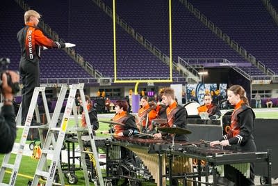 A marching band performs on the field of a football stadium.