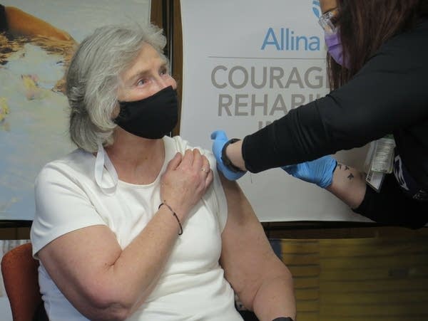 A woman wearing a face mask receives a vaccine shot.