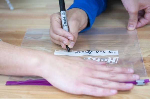 A teen uses a marker to write "Makenna" on a ziplock bag. 