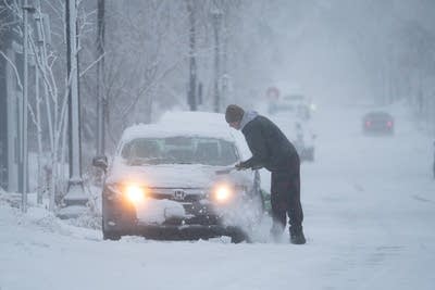 A person clears off snow on a car 