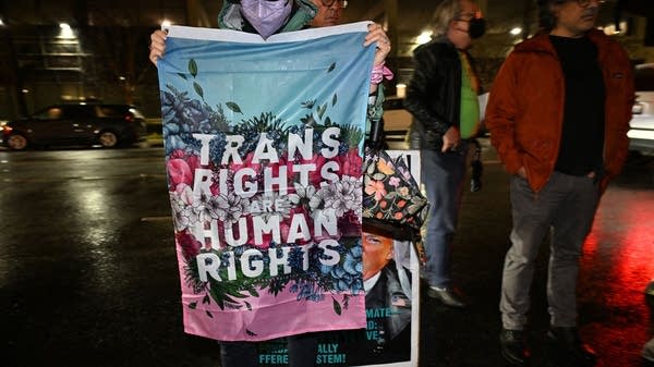 A person holds a pink and blue flag that says "Trans rights are human rights."