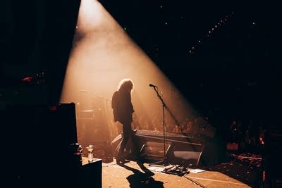 A guitarist performing in a spotlight onstage in a large music venue